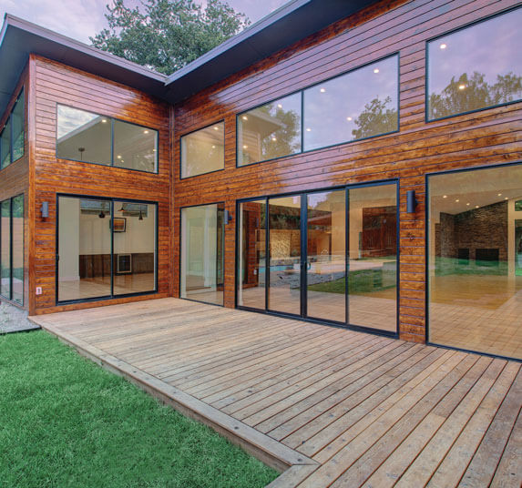 Modern wood clad home with large black framed windows and sliding doors opening onto a wooden deck.