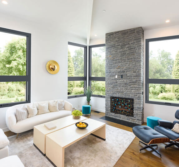 Bright living room with a stacked stone fireplace, curved white sofa and black leather lounge chair.