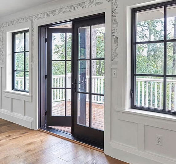 Open black French doors leading to a wooden deck between white paneled walls and black framed windows.