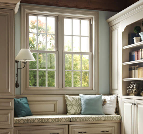 Built in window seat with teal and cream pillows flanked by cabinetry and bookshelves beside a wall sconce.