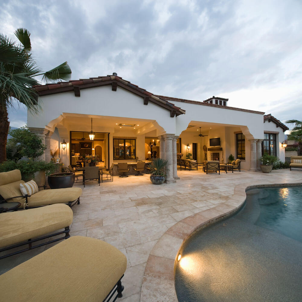 Mediterranean style home with an illuminated open air living space overlooking a curved swimming pool at dusk.